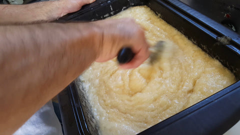 A man's arm stirring soap, that's cooking in a roaster, with a large spoon.