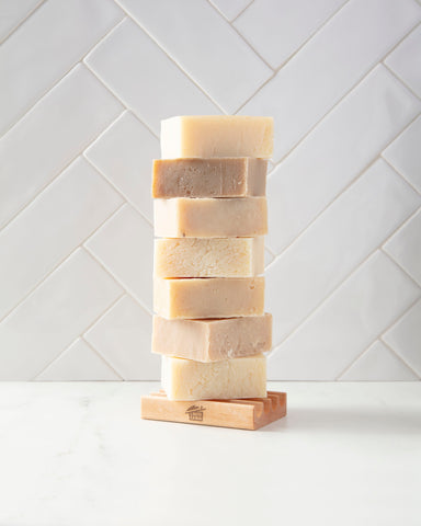 Stack of The Mod Cabin soap sitting on wooden soap on a white counter with a white subway tile backsplash.